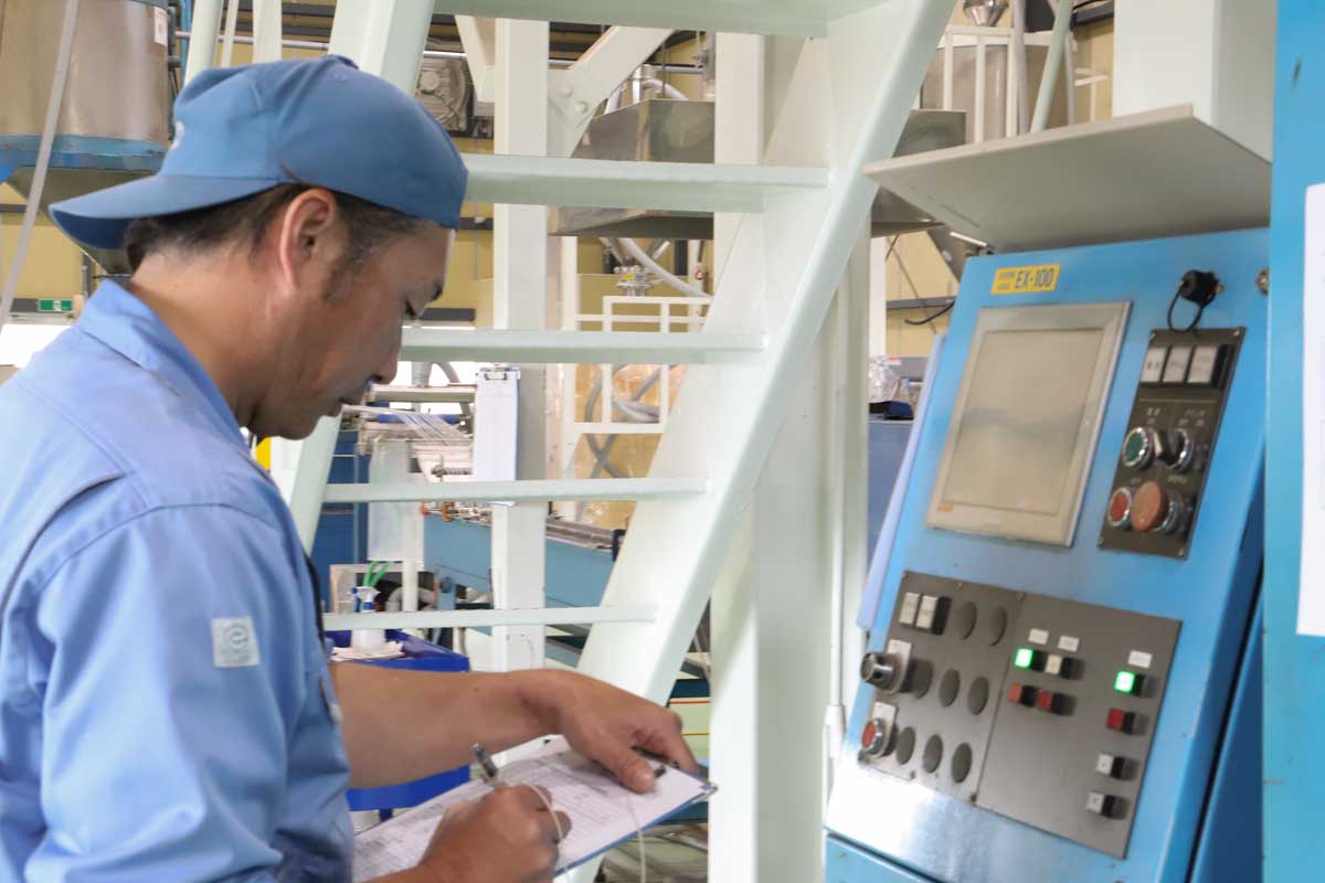 工場の機械のそばで記録を確認する相和の社員
